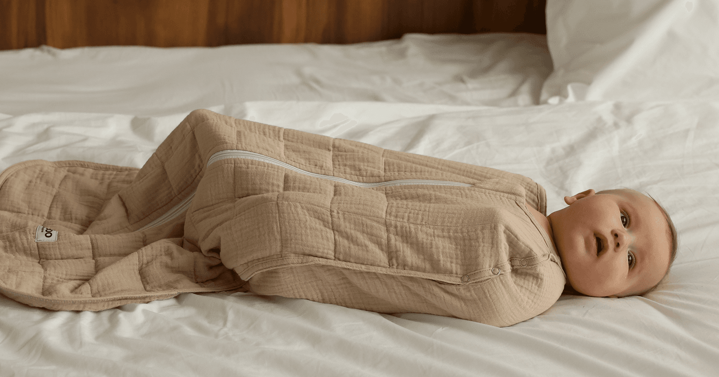 Baby swaddled in a Lullaboo weighted sleeping bag, lying on a bed