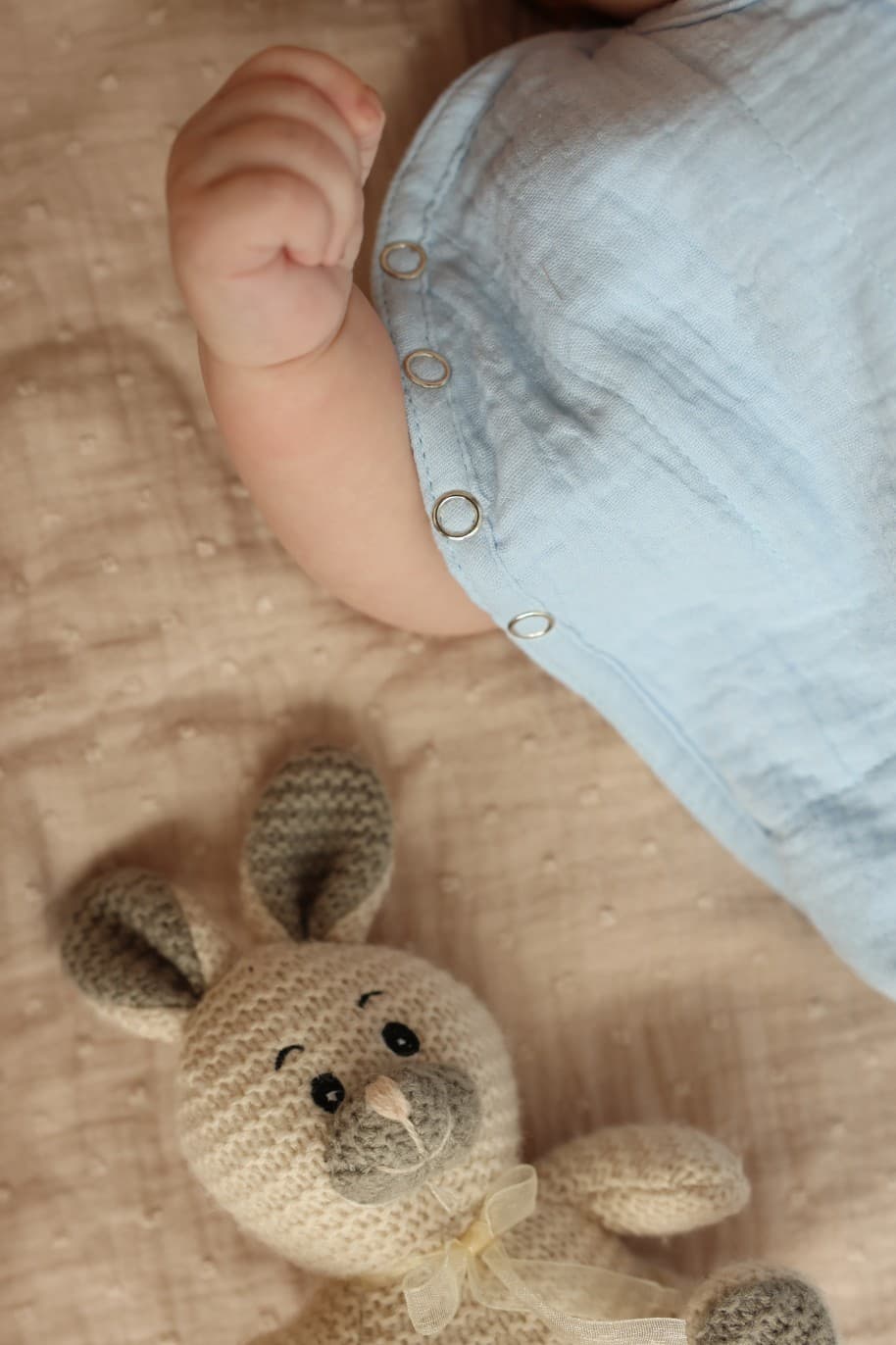 Baby's foot resting beside a knitted bunny toy on a muslin blanket
