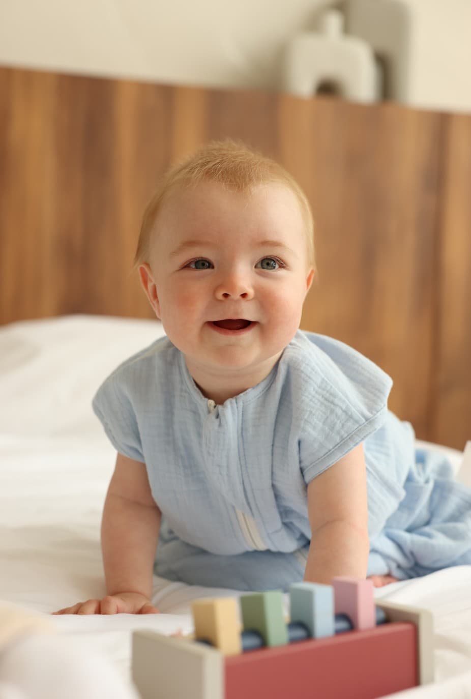 Baby crawling on a bed and smiling next to a wooden toy block set