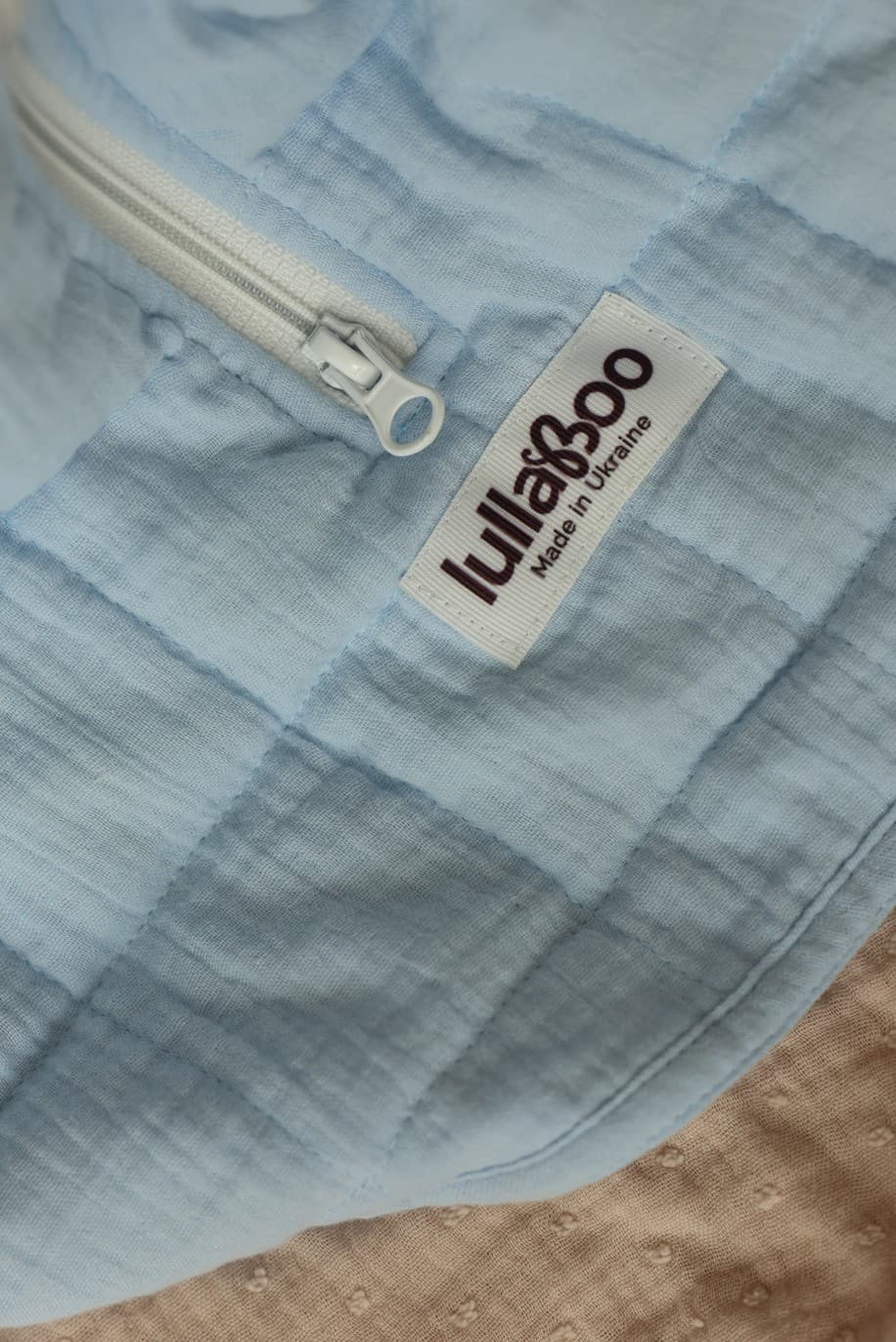 Close-up of the Lullaboo woven label and zipper pull on a quilted blue sleeping bag