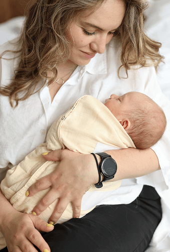 Mother in a white shirt gently cradling her swaddled newborn baby